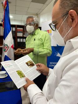 Jefrey Lizardo leyendo el folleto de la Flor de Bayahibe entregada en el acto de firma de convenio entre CONADIS y SIUBEN 